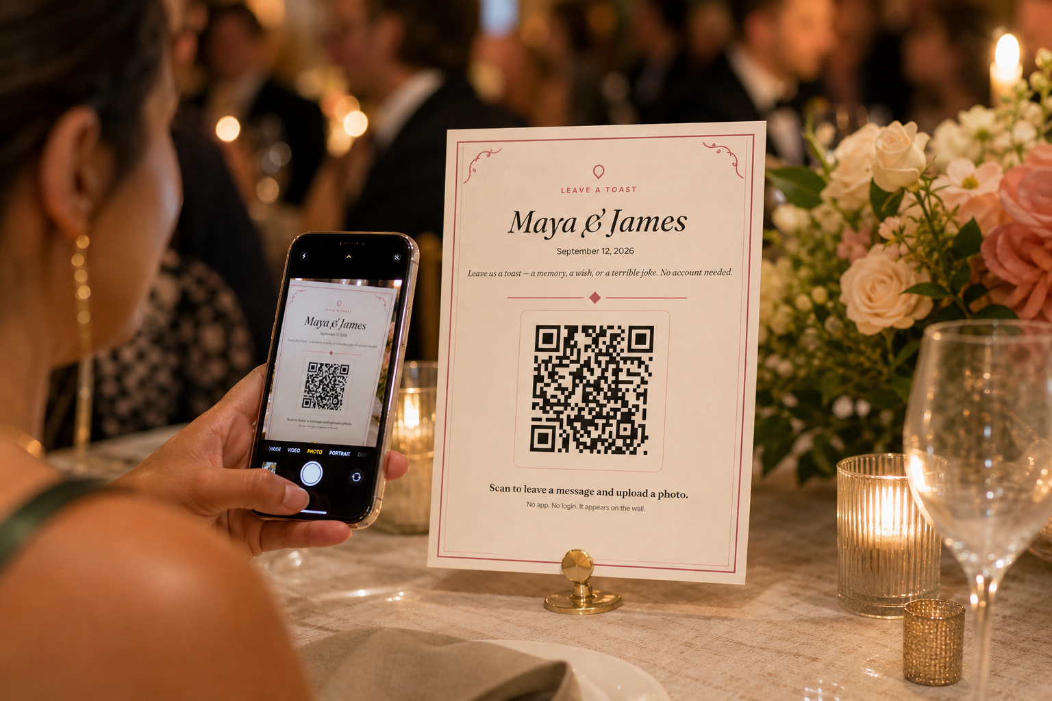 A wedding guest holds a phone over a Willow Book table sign, scanning the QR code while the reception continues behind them